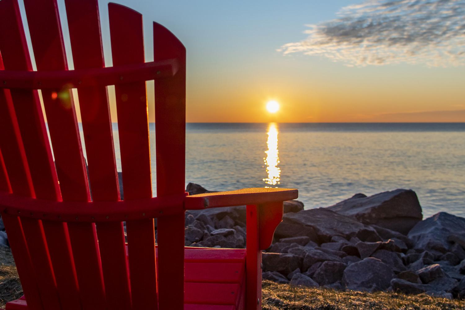 一张红色的阿迪朗达克椅子，面对着日出时的湖面.